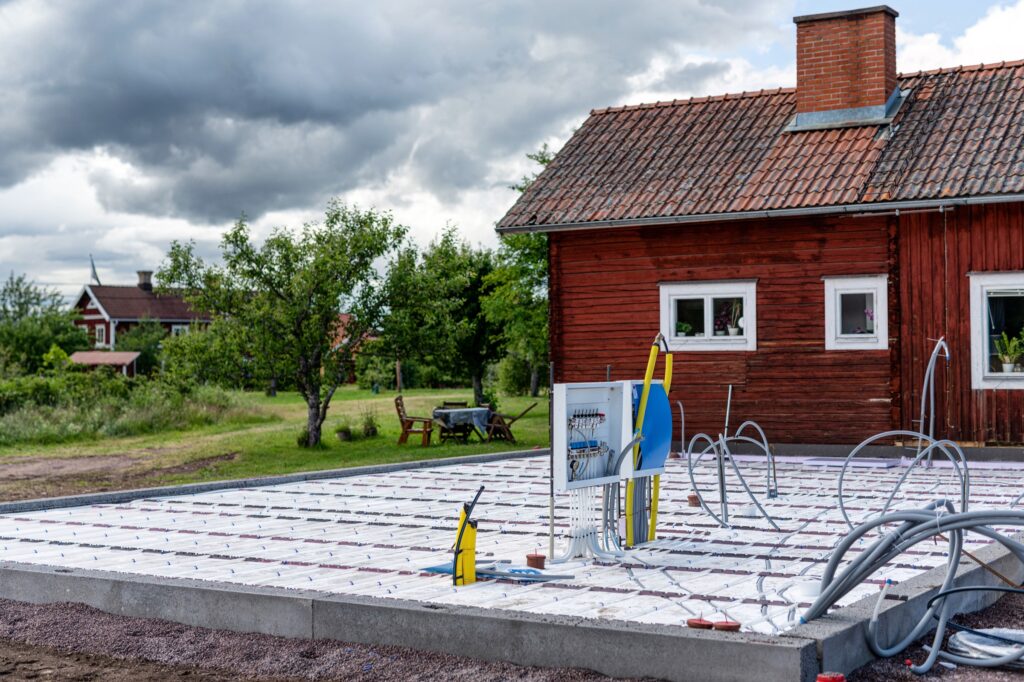Husplatta med golvvärmeslingor och fördelare framför ett faluröd hus
